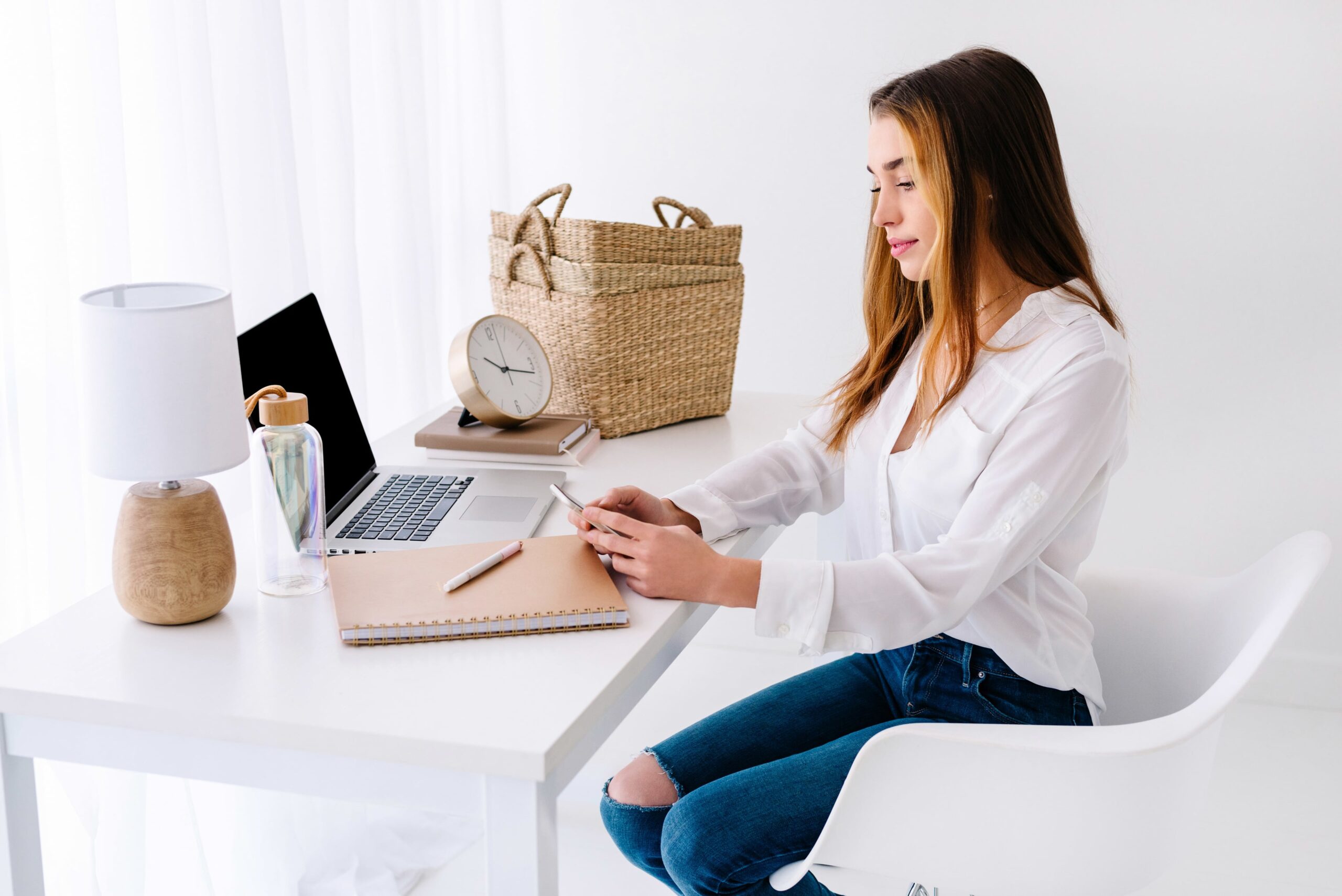 jeune femme assise à son bureau avec son ordinateur portable et son téléphone à la main